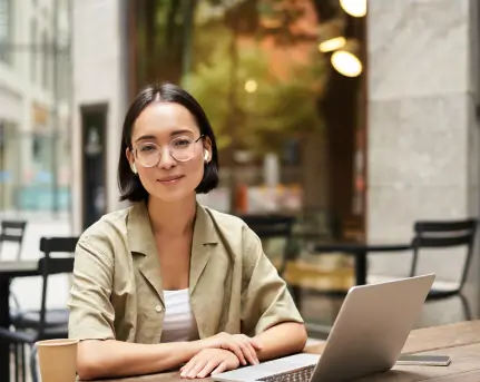 young-woman-student-working-from-cafe-sitting-with-laptop-cup-coffee-outdoors-looking